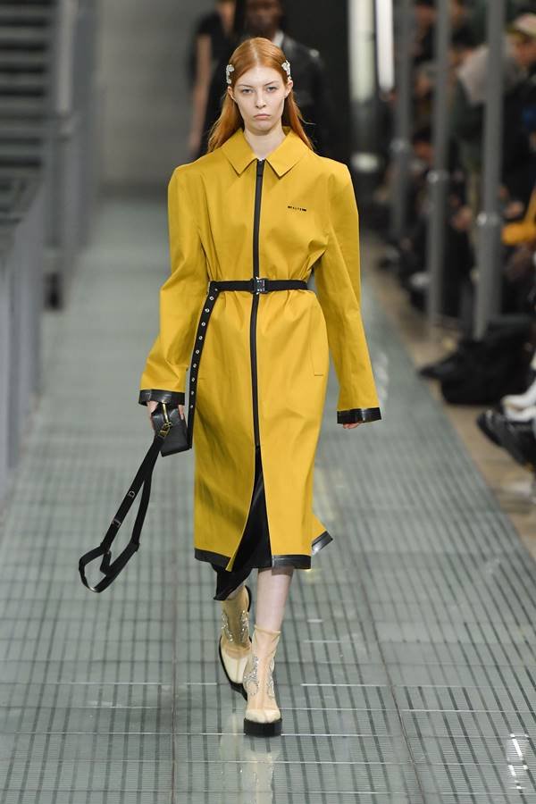 Modelo desfilando com casaco amarelo da marca 1017 ALYX 9SM