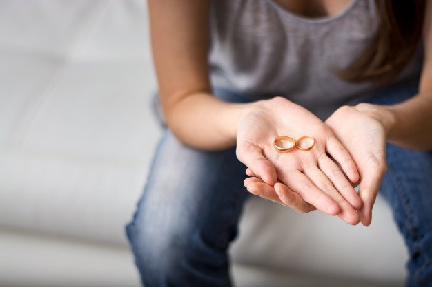 pessoa com as mãos estendidas para frente segurando duas alianças douradas