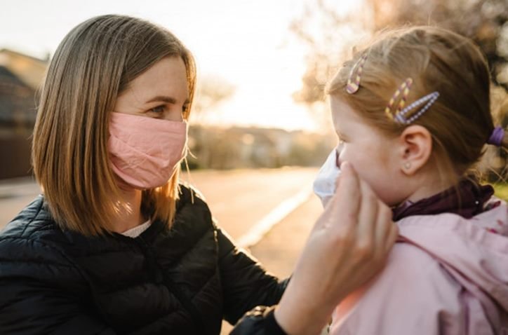 Mãe colocando máscara de proteção na filha uma menina