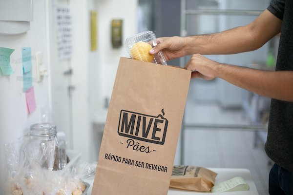 Mão colocando pães embalados em uma sacola de papel