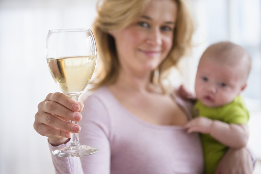 Mulher segura taça de vinho e bebê