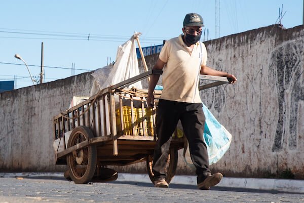 Homem puxando carrinho com materiais recicláveis em frente a muro