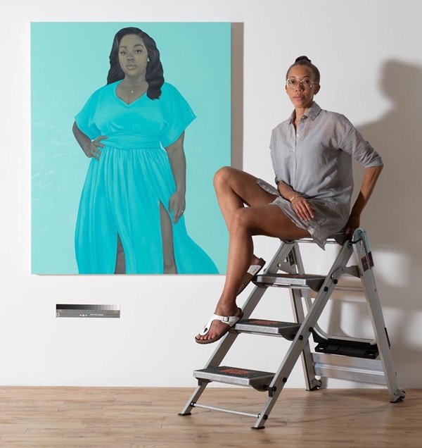 Amy Sherald sentada em escada, ao lado de pintura com o rosto de Breonna Taylor