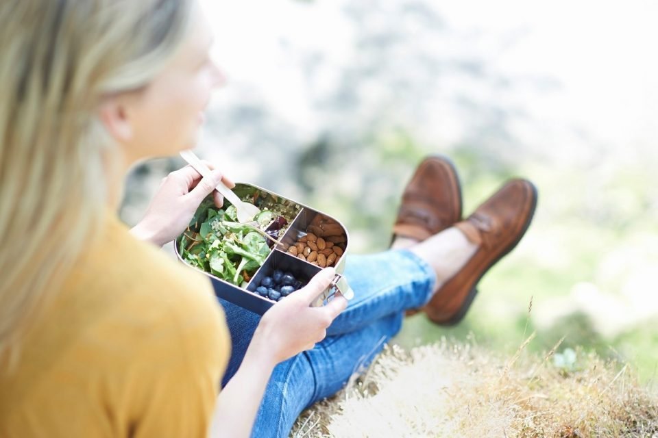 mulher sentada na grama comendo alimentos saudáveis