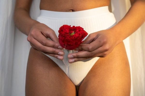 Mulher com calcinha branca e cravo vermelho nas mãos faz metáfora visual da menstruação
