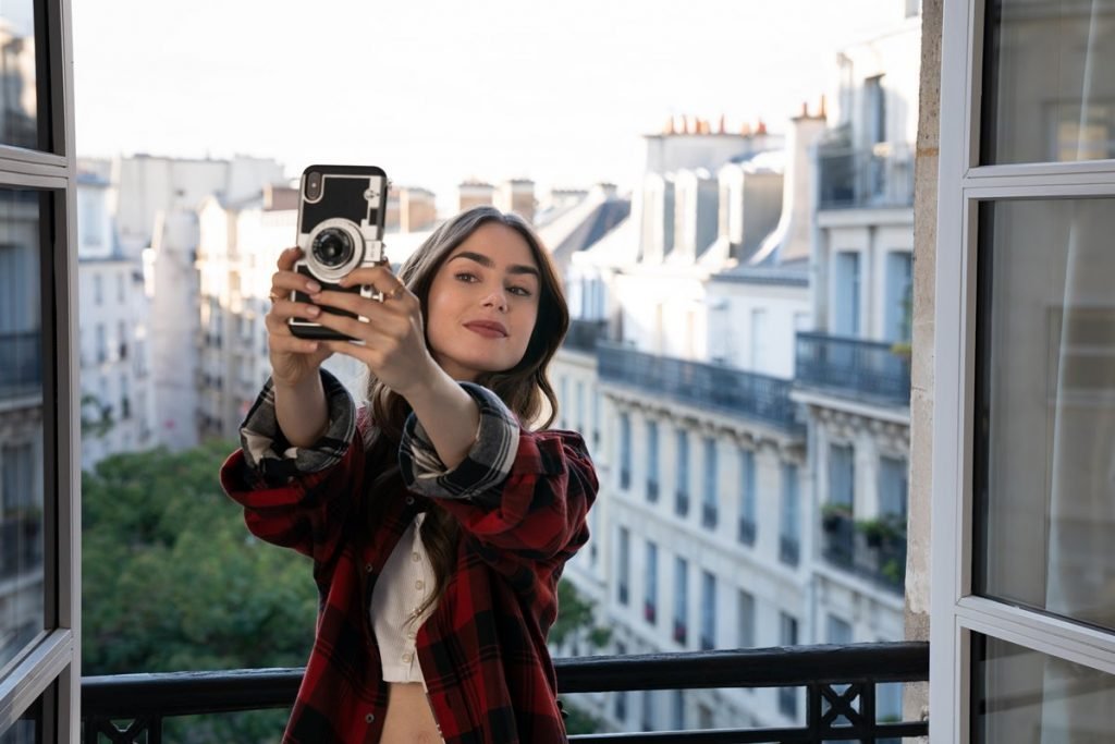 Lily Collins tirando selfie na sacada, em trecho da série Emily in Paris