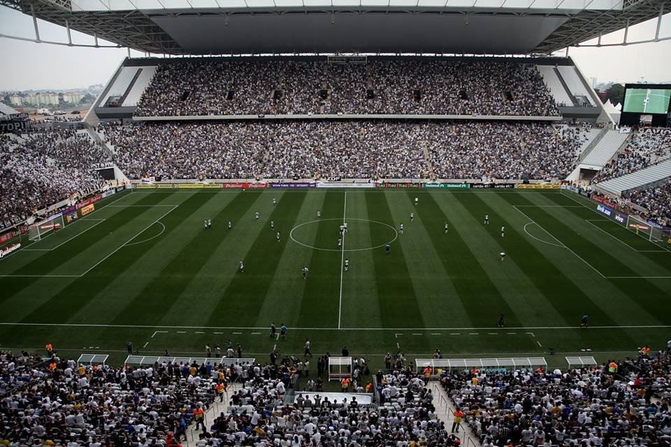 Imagem colorida mostra o estádio do Corinthians, em Itaquera. O campo está com os jogadores posicionados para o início de um jogo e as arquibancadas estão cheias de torcedores - Metrópoles