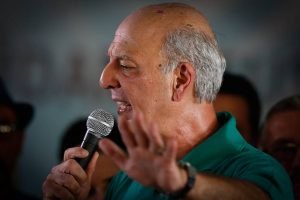 Homem fala ao microfone com a mão levantada