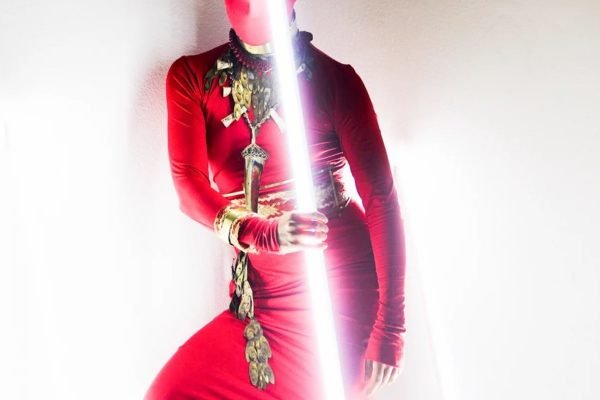 Modelo usa vermelho, com joias, e segura um sabre de luz