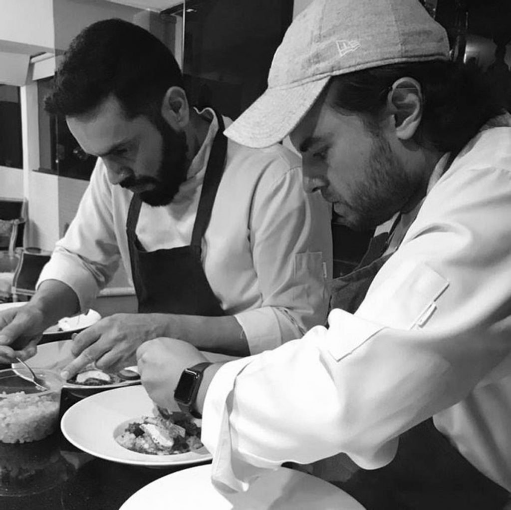 Chef Diego Badra e Chef Igor Janiques, dois homens montam pratos na cozinha de um restaurante