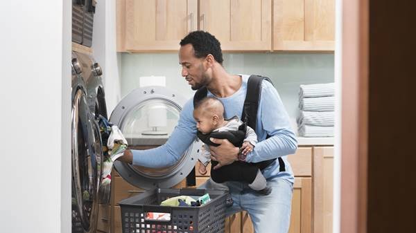 Pai com filho no colo lavando roupas