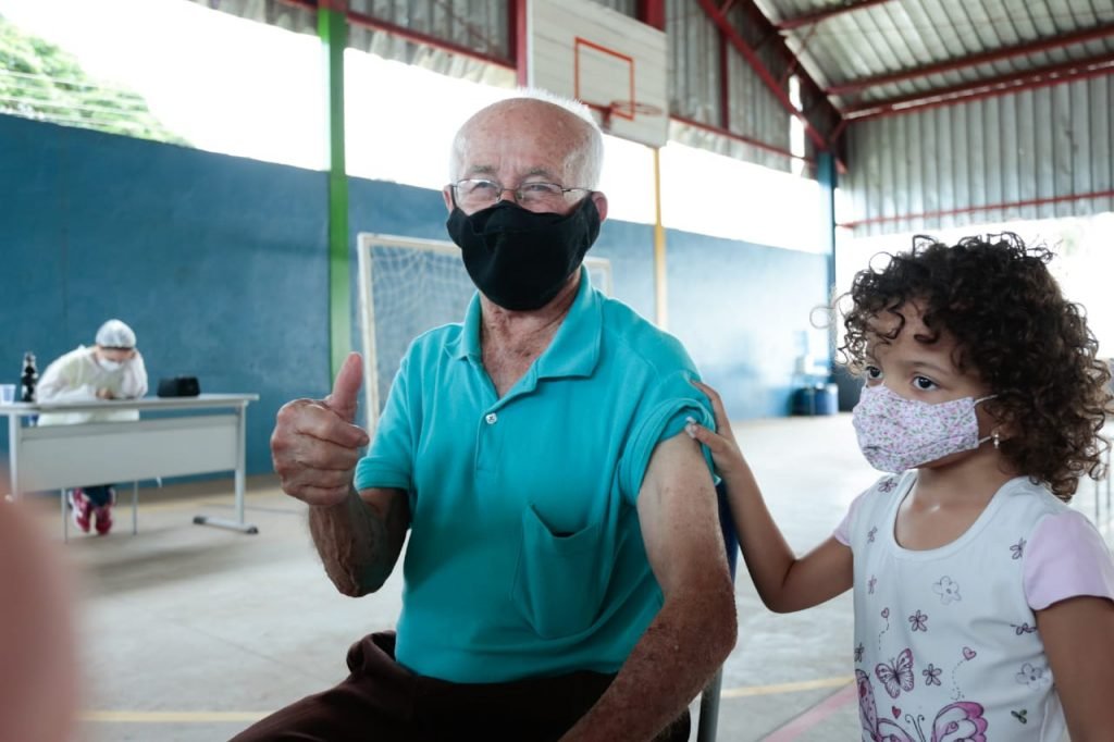 Neta fica ao lado do avô na hora vacina contra a covid-19 em Goiânia