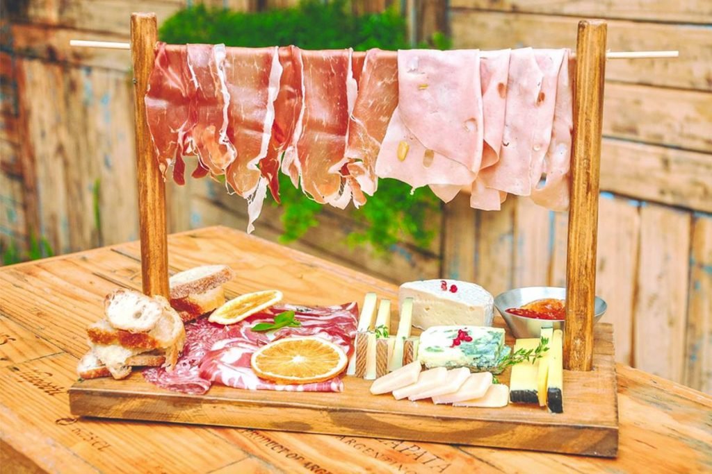 tábua com queijos, embutidos, frutas e varal com embutidos