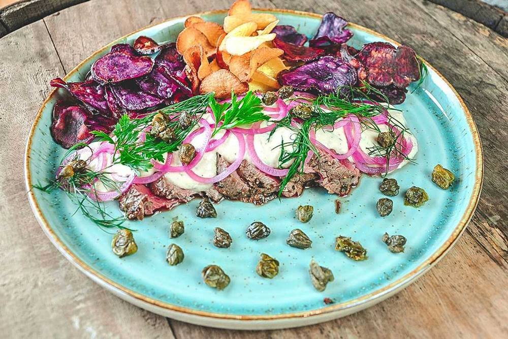 Prato azul com carne, molho e chips de mandioca e batata doce roxa