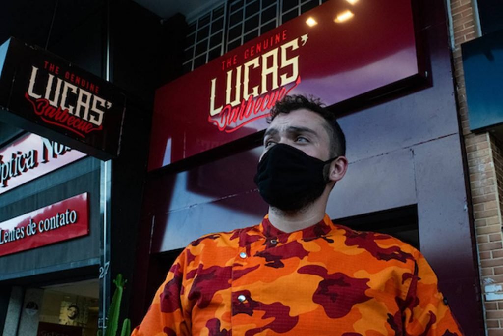 Homem de máscara olha para o horizonte em frente a fachada do restaurante Lucas Barbecue