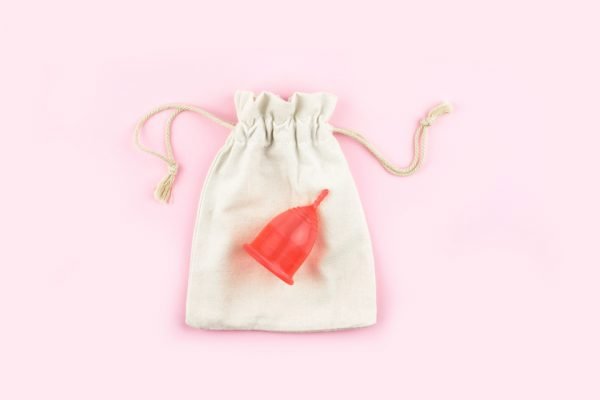 Saquinho branco em fundo rosa e coletor menstrual vermelho em cima
