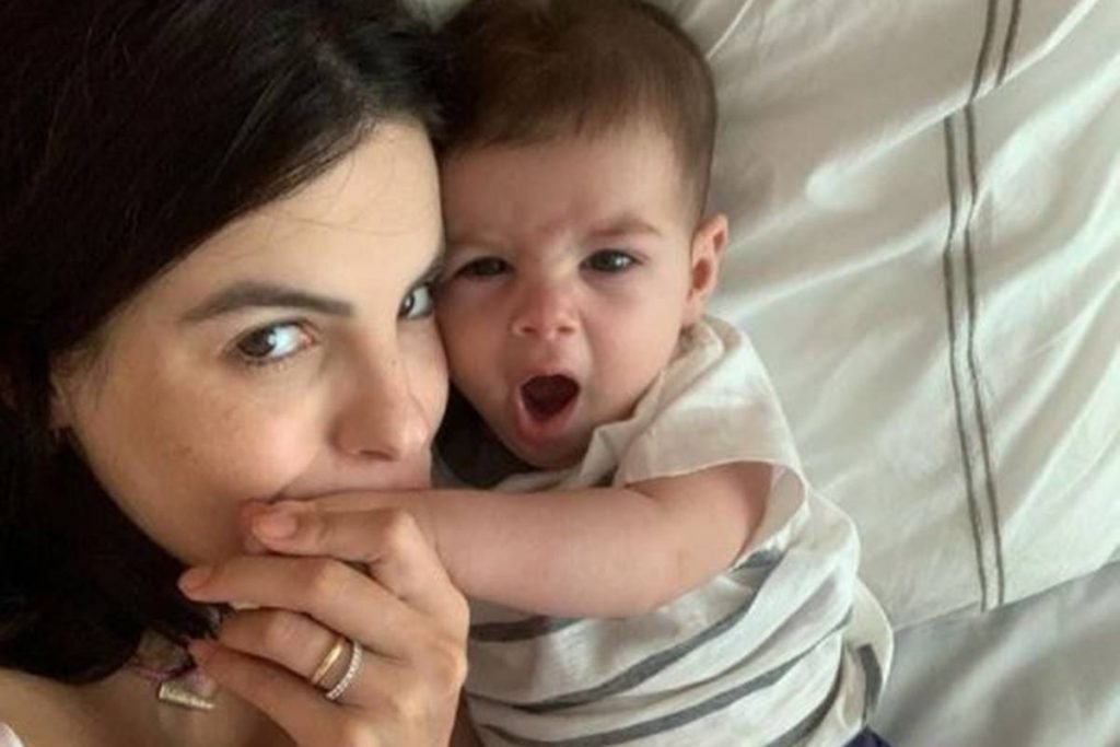 Mulher beija a mão de bebê enquanto ele boceja