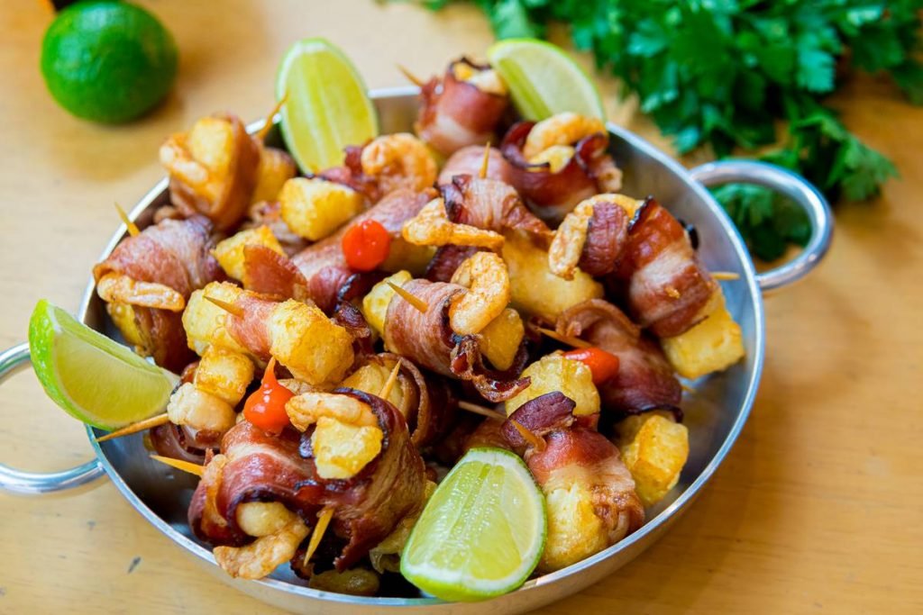 Panela de metal com espetos de camarões enrolados no bacon e fatias de limão nos cantos