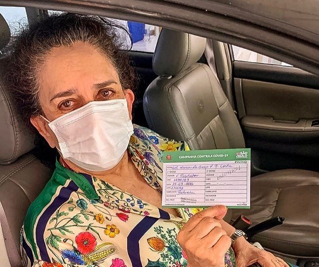 Gal Costa recebendo a vacina contra a Covid-19, segurando o cartão de vacinação