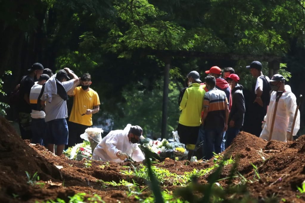 Imagem colorida de diversas pessoas no cemitério da Vila Formosa, em São Paulo, acompanhando enterro - Metrópoles
