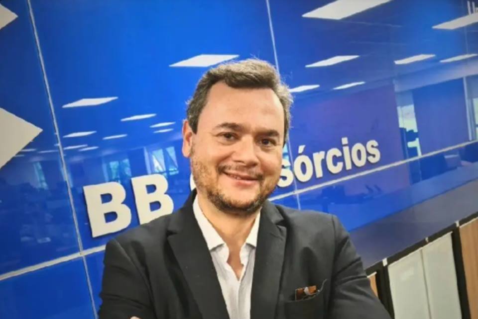 Fotografia colorida de homem de terno, com braços cruzados e sorrindo