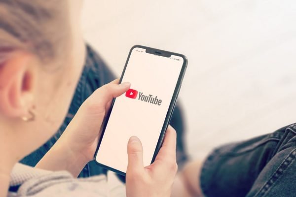 mulher segura celular e na tela aparece a logo do YouTube