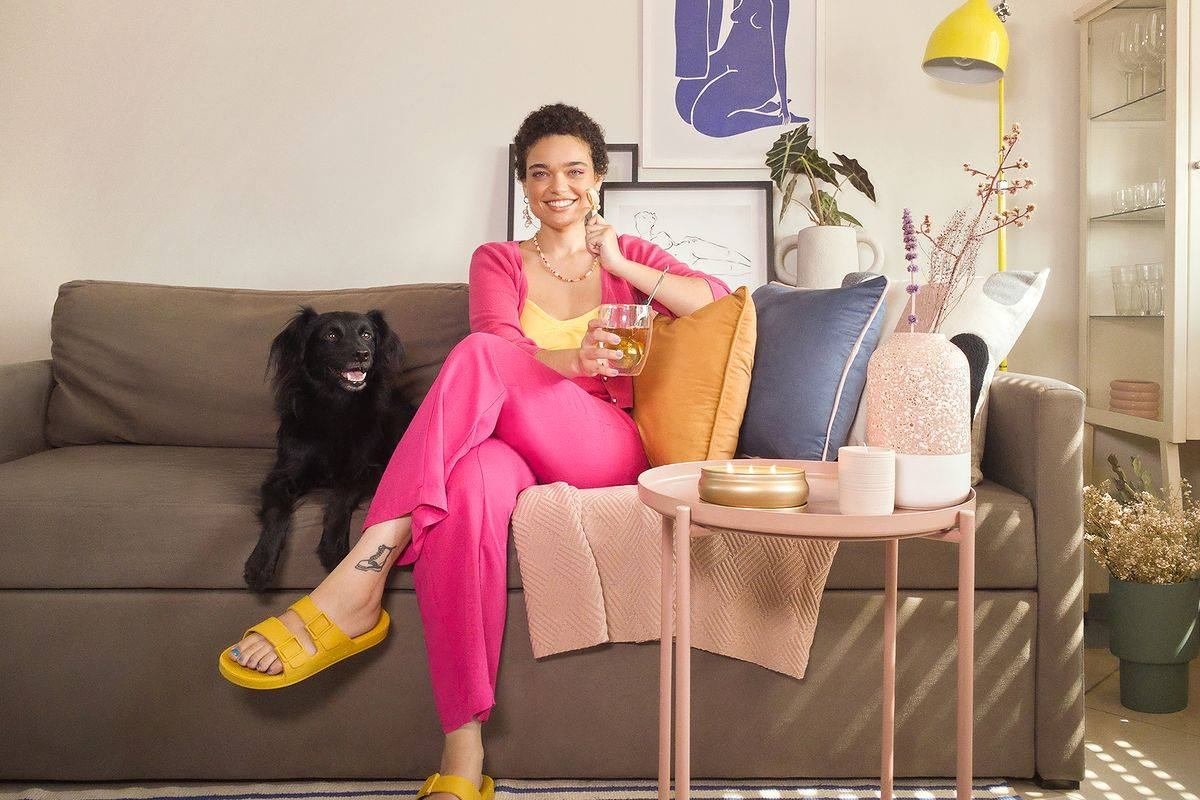 Mulher sentada no sofá com cachorro, em campanha da Amaro