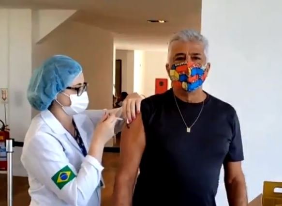 Lulu Santos sendo vacinado contra a Covid-19 no Rio, por profissional de saúde, de máscara