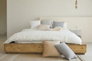 cama baixa com lençóis brancos e almofadas espalhadas