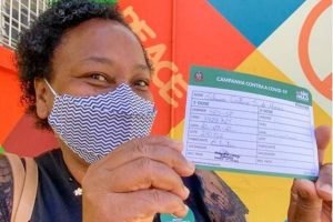 Merendeira Silmara Moraes com cartão de vacina após receber primeira dose de vacina contra a Covid-19