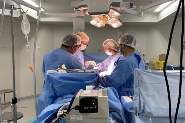 Fotografia colorida de centro cirúrgico com profissionais ao redor da maca