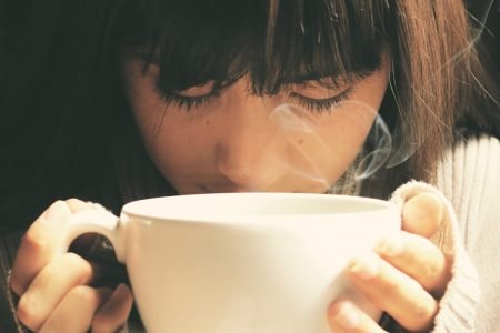 menina cheirando xícara de café