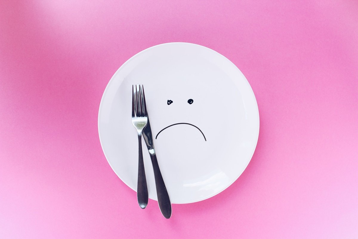 Imagem de prato branco com talheres em cima e sorriso triste desenhado - Metrópoles
