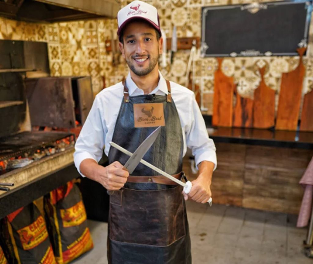 Netão Bom Beef com avental de couro afiando faca