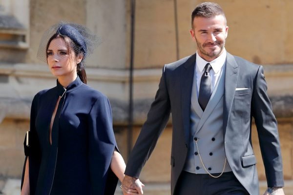 Foto colorida de David e Victoria Beckham de mãos dadas, vestidos com roupa social em evento - Metrópoles