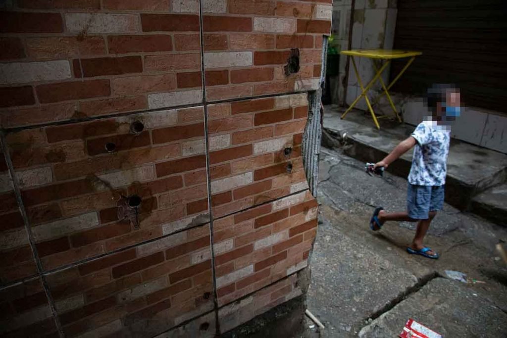 Criança passa perto de parede com marcas de tiros no Jacarezinho