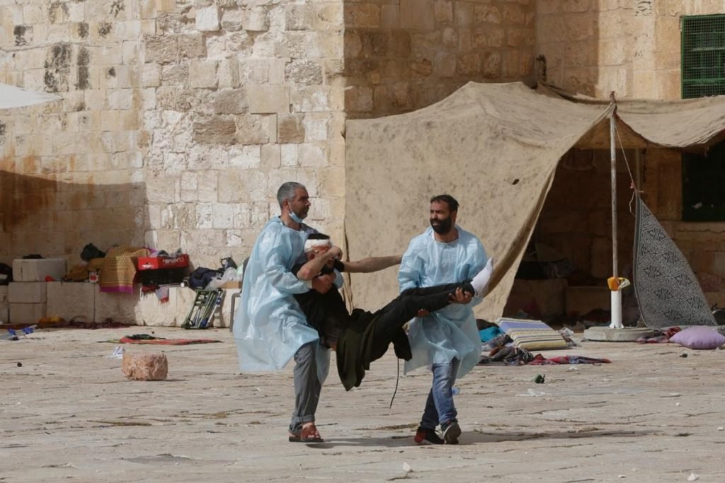 Homens carregam um ferido durante confronto entre as forças de segurança israelenses e palestinos em frente à Mesquita Cúpula da Rocha, no complexo da Mesquita de Al Aqsa, na Cidade Velha de Jerusalém, em Israel