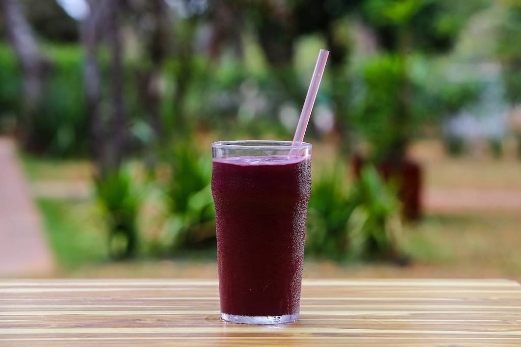 Copo com suco de uva e canudo de plástico em cima de mesa de madeira