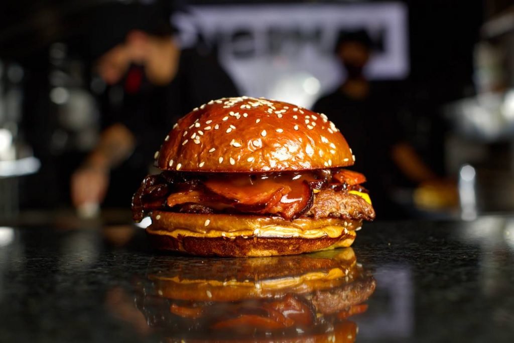 Sanduíche com carne, queijo, bacon no pão com gergelim e cozinha ao fundo