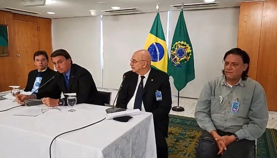 Reunião de Jair Bolsonaro com médicos, na qual ouve ressalvas às vacinas; na mesa, Osmar Terra ao lado de Bolsonaro, com o virologista Paolo Zanoto sentado à direita, na foto, de camisa cinza e cabelos longos