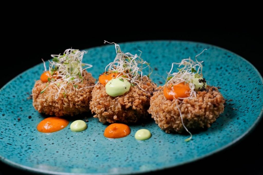 Prato com três croquetes de cupim e gotas de molhos