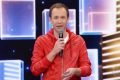 Tiago Leifert de blusa de frio laranja com microfone na mão no programa Domingão
