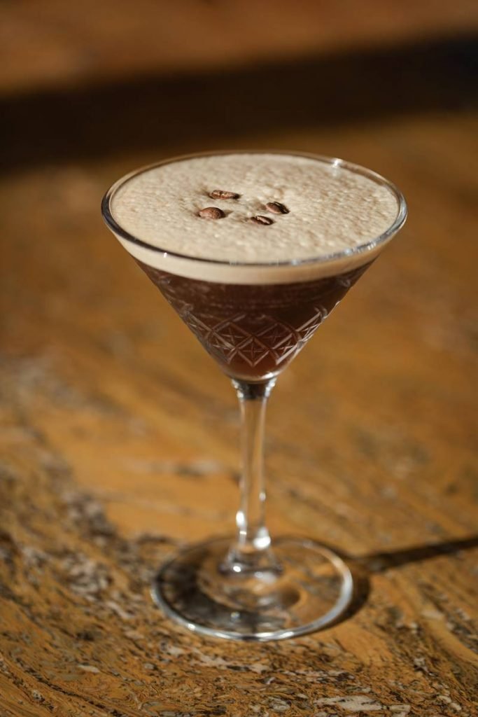 Copo com drinque cor de café, espuma e grãos de café em taça martini