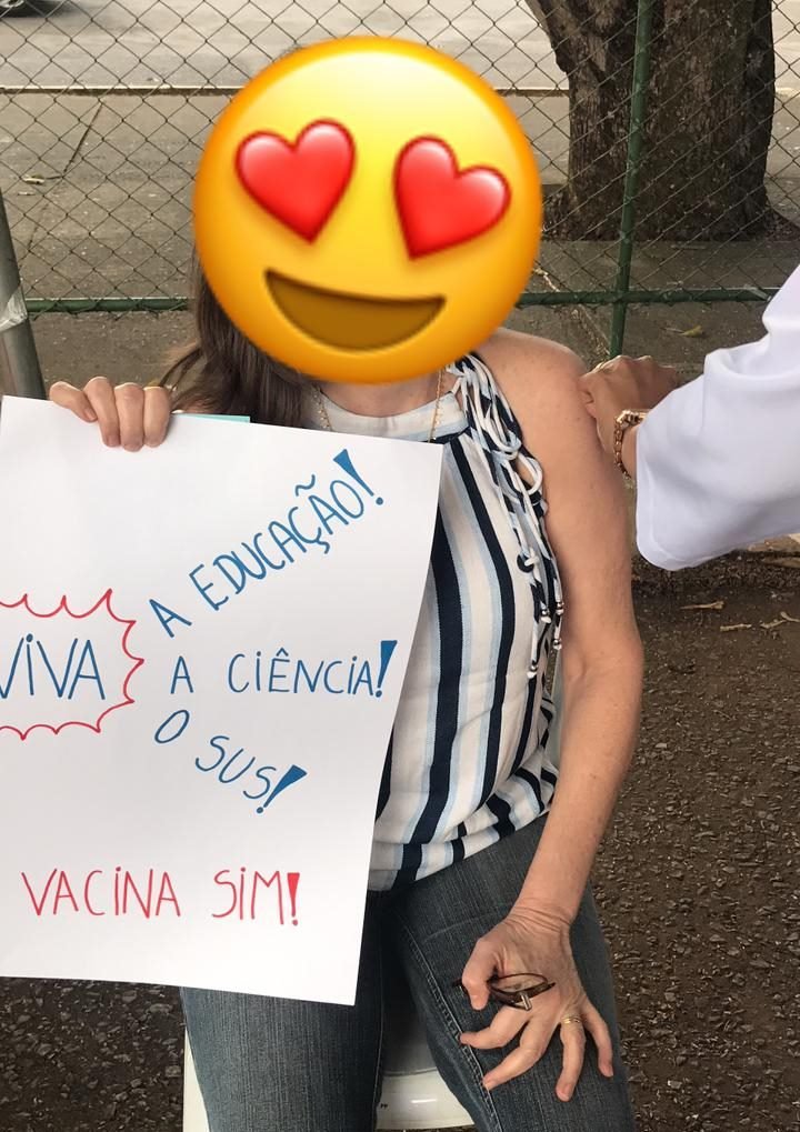 Mulher segurando cartaz enquanto se vacina