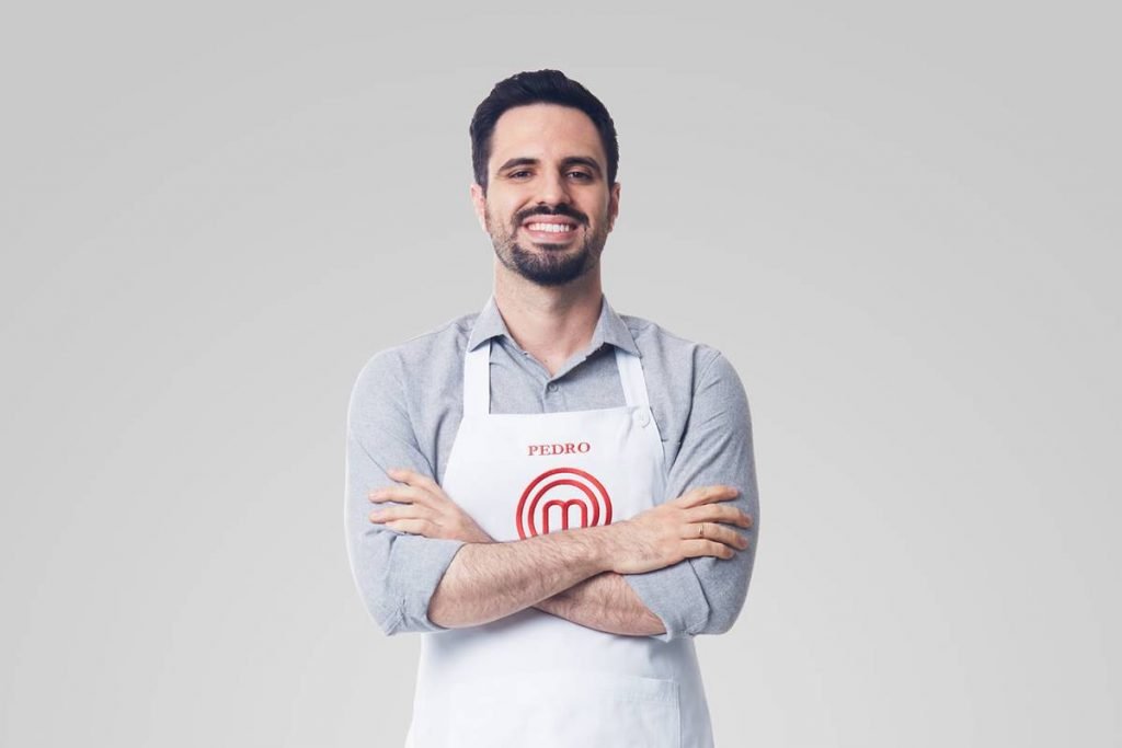 Homem posa com avental do masterchef de bra&ccedil;os cruzados e sorri