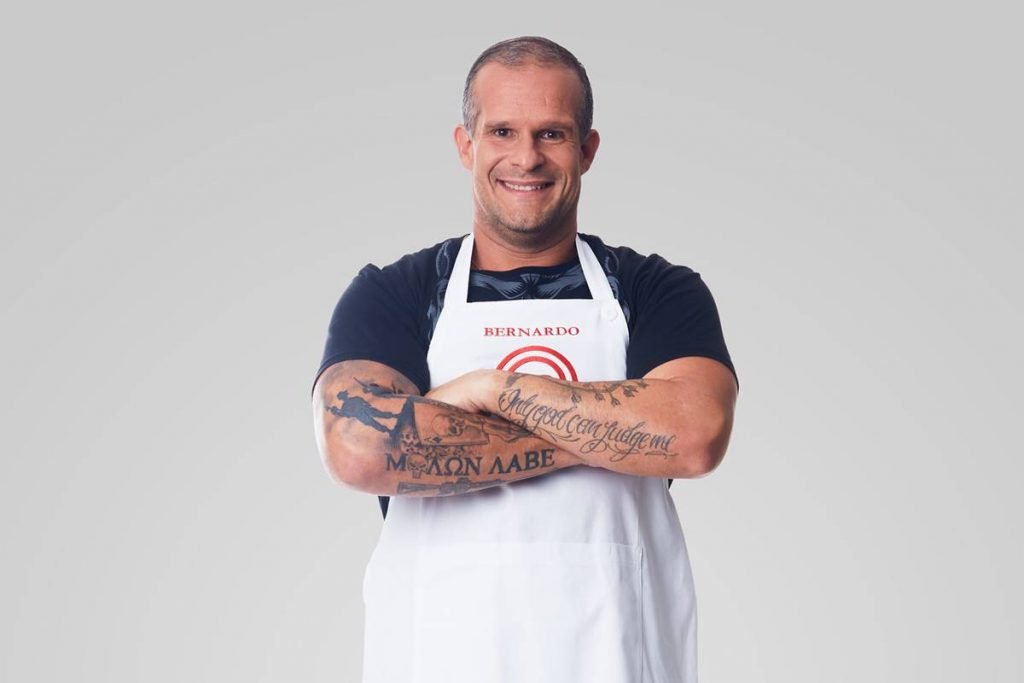 Homem posa com avental do masterchef de bra&ccedil;os cruzados e sorri