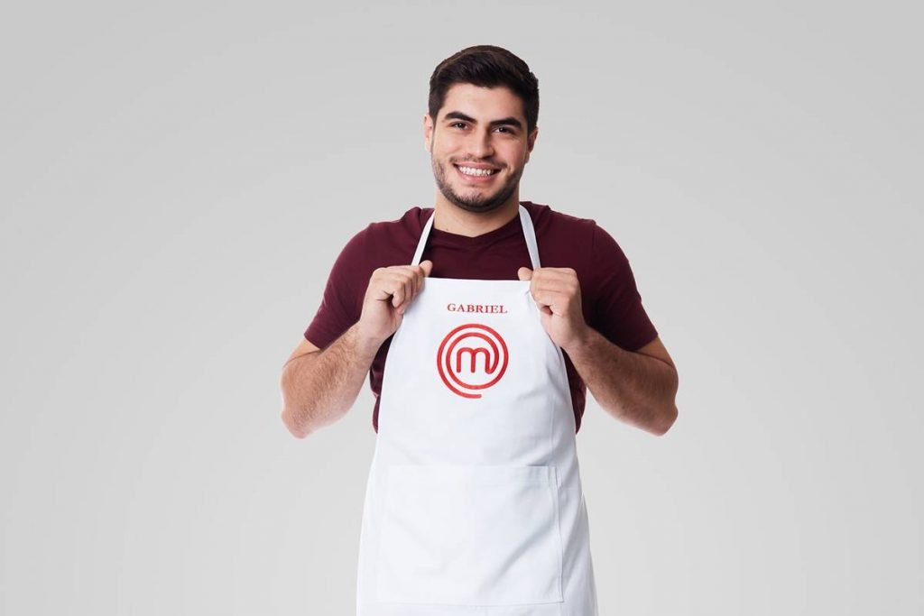 Homem sorri segurando avental do masterchef