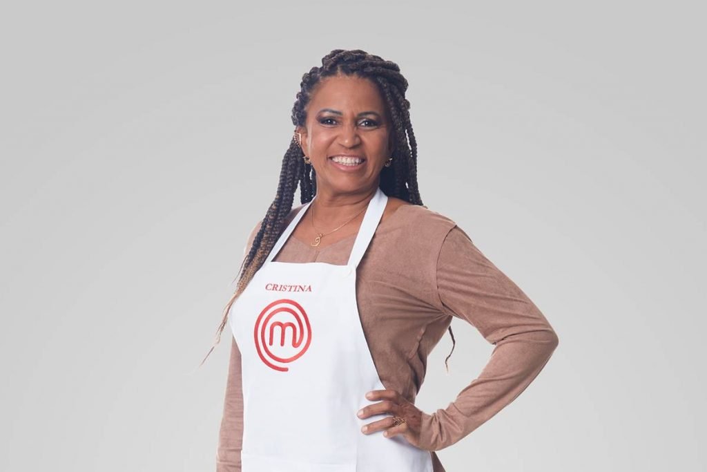 Mulher de blusa de manga longa marrom posa com mão na cintura e sorri