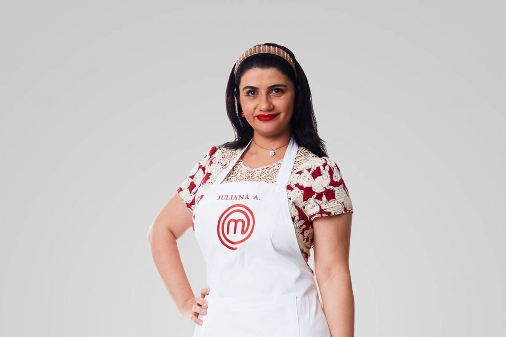 Mulher posa de vestido estampado, tiara e avental do masterchef com mão na cintura
