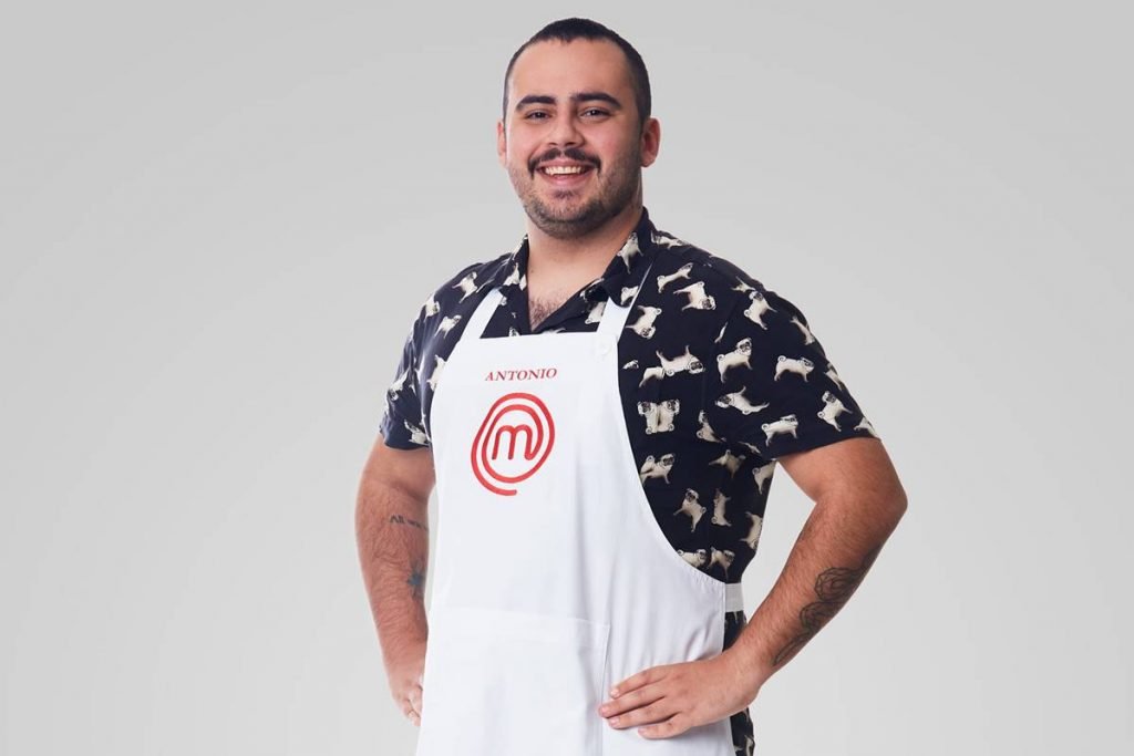 Homem posa de avental do masterchef e camisa estampada de manga curta